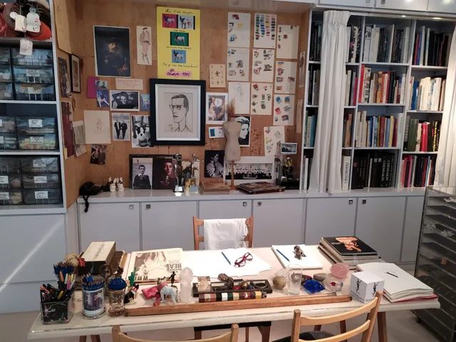The studio of fashion designer Yves Saint Laurent at the Musée Yves Saint Laurent Paris. The desk is covered with sketches, art supplies, and books, while the walls display fashion drawings, photographs, and portraits, including a Bernard Buffet drawing and a photograph of Catherine Deneuve. Four kinds of local business support a creative retreat can use